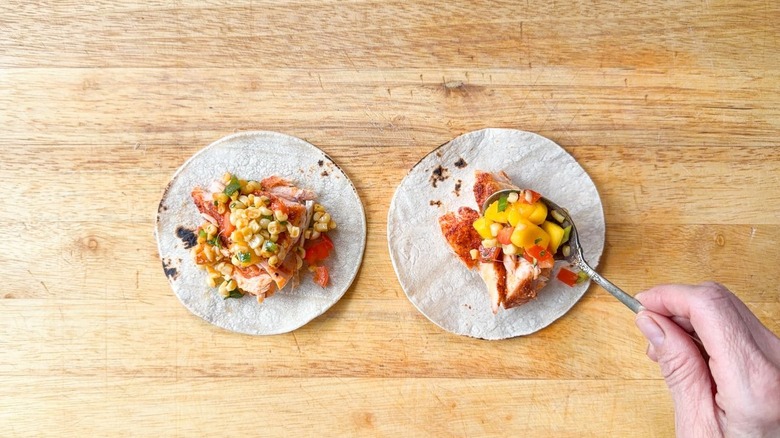 Spooning mango-corn salsa onto baked salmon chunks on white corn tortillas