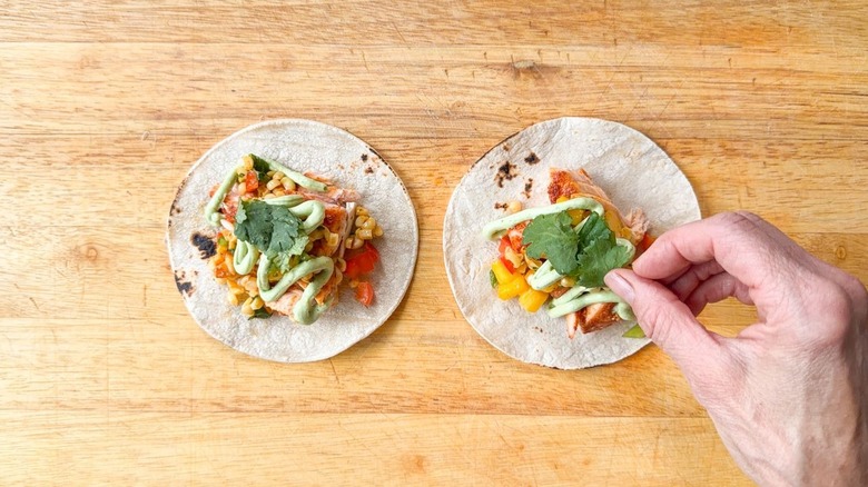 Adding cilantro leaf garnish to slow-baked salmon tacos with mango-corn salsa