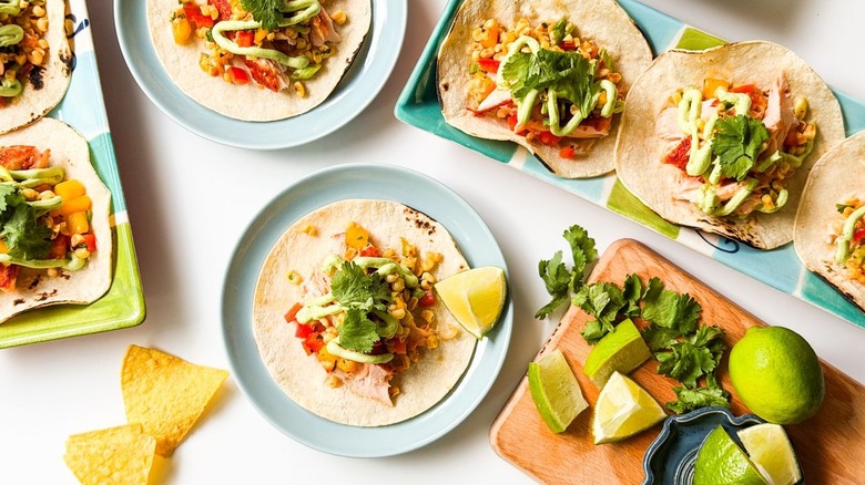 Slow-baked salmon tacos with mango-corn salsa on serving platters and plates with lime wedges on side