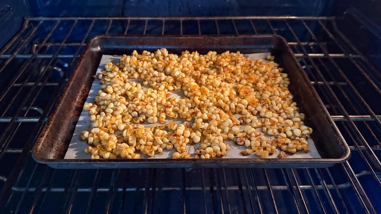 Seasoned corn kernels roasting on parchment-lined baking sheet in oven