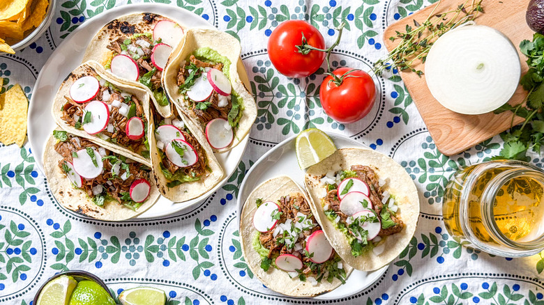 Slow cooker barbacoa tacos on platter and serving plate with garnishes, chips, and beer