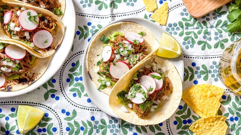 Slow cooker Barbacoa tacos on plate and platter with lime wedges