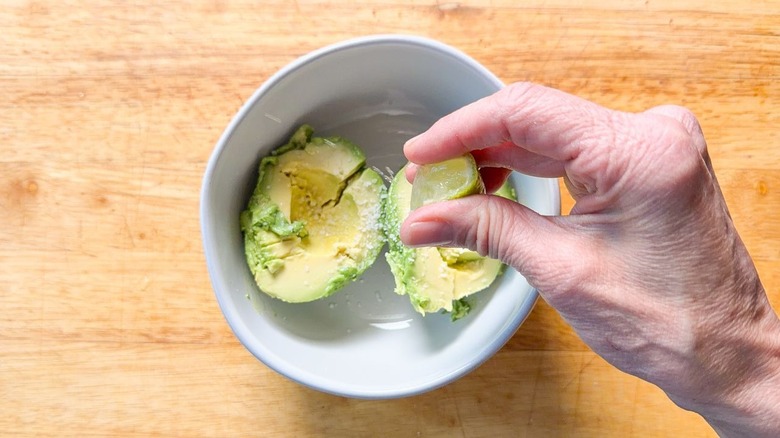 Squeezing fresh lime over avocado flesh in bowl