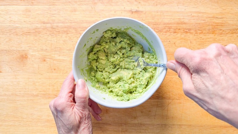 Mashing avocado flesh in bowl with fork