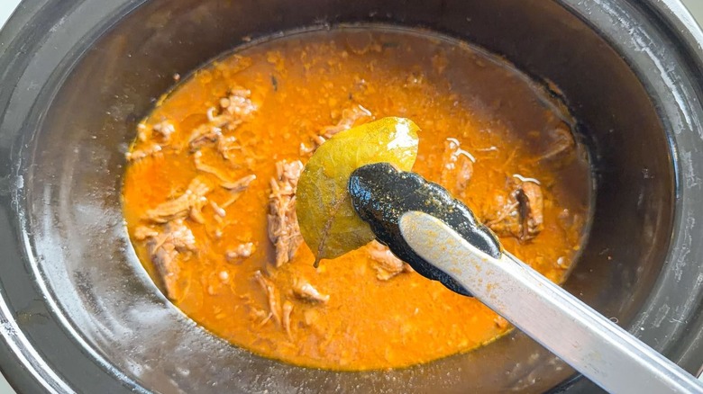 Using tongs to remove a bay leaf from barbacoa beef in slow cooker