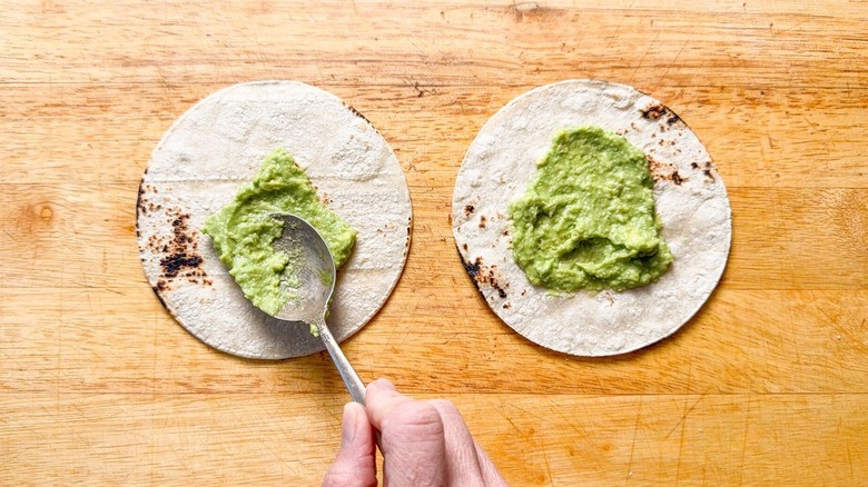 Using a spoon to spread mashed avocado on corn tortillas