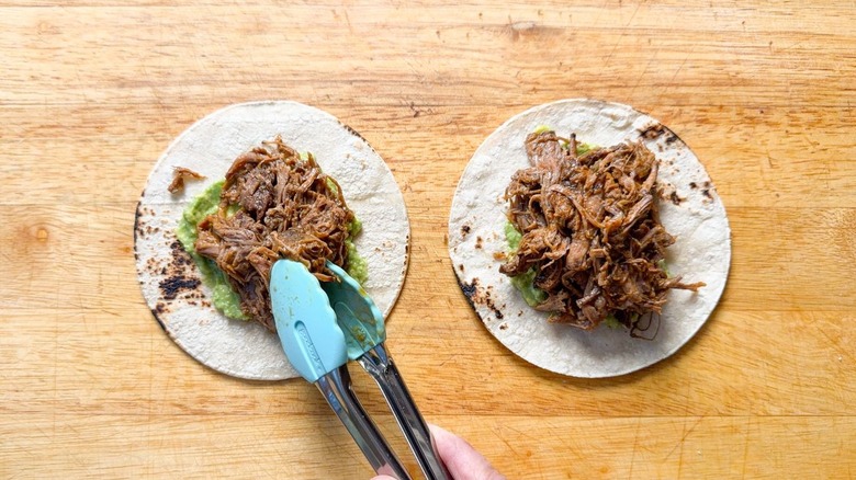 Adding barbacoa beef to corn tortillas with mashed avocado