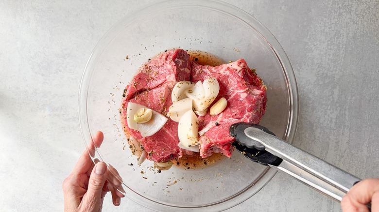 Turning beef chuck in marinade in glass bowl with tongs