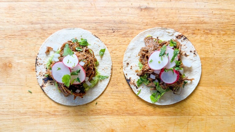 Slow cooker barbacoa tacos garnished with chopped onion, radish slices, and cilantro