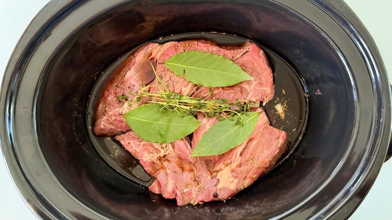 Marinated beef chuck with beef stock, fresh bay leaves, and fresh thyme in slow cooker