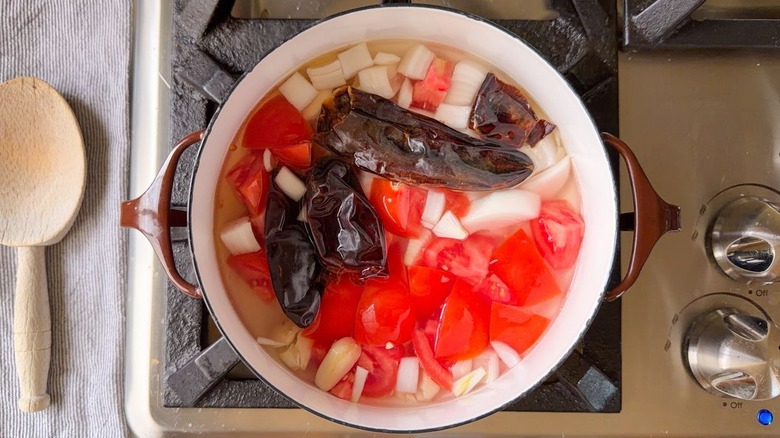 Dried chilies, tomatoes, onion, and garlic in water in pot on stovetop