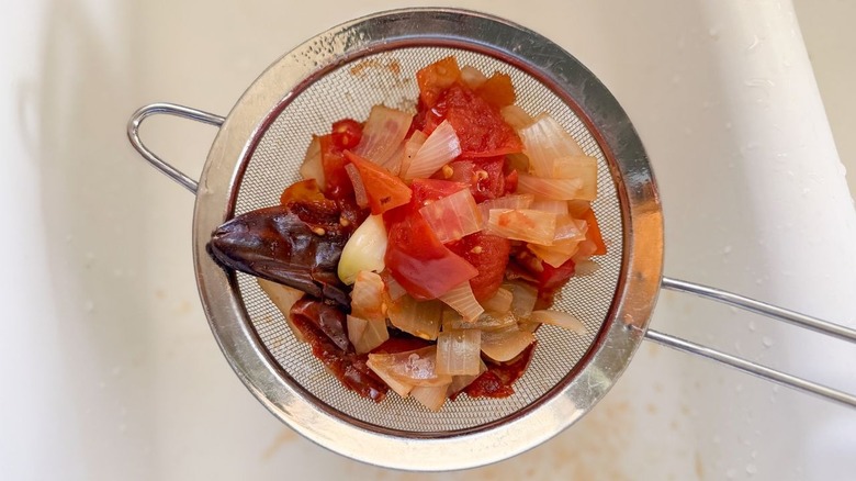 Cooked reconstituted chilies, tomatoes, onion, and garlic in strainer over sink
