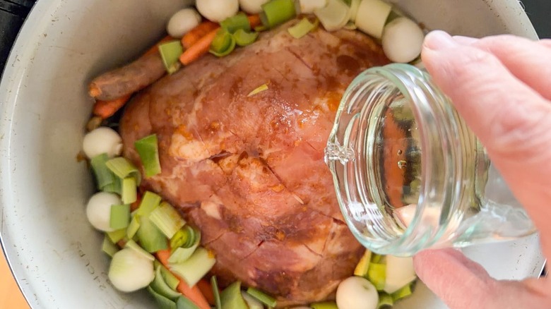 Pouring white wine over Kahlua apricot glazed ham with baby vegetables in slow cooker