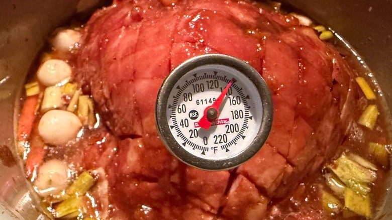 Instant read thermometer at 140 F inserted into glazed ham in slow cooker