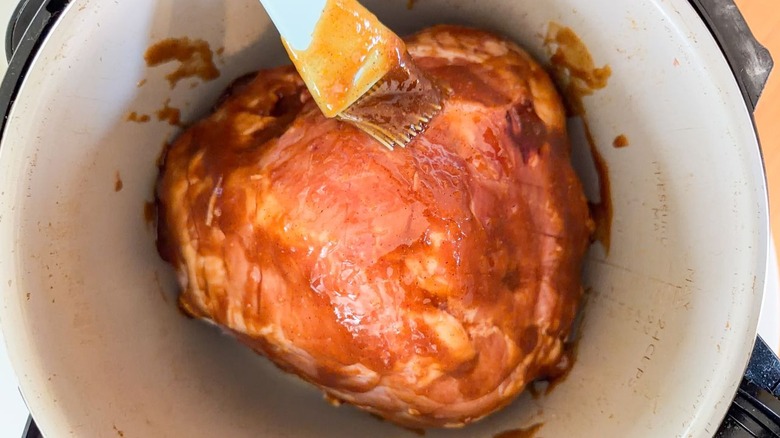 Brushing Kahlua apricot glaze onto ham in slow cooker