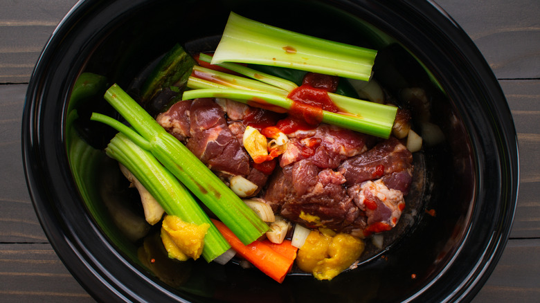 Raw meat and vegetables in a black slow cooker.