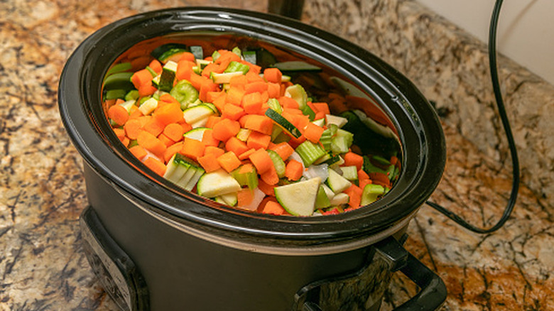 Vegetables in a black slow cooker on granite countertop.