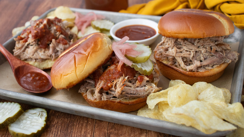 Side shot of pulled pork sandwich with sauces and pickles