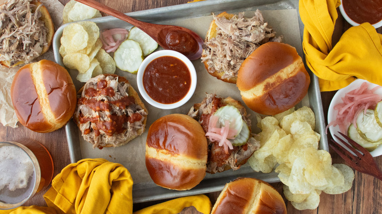 Overhead shot of several pulled pork sandwiches with sauce and pickles