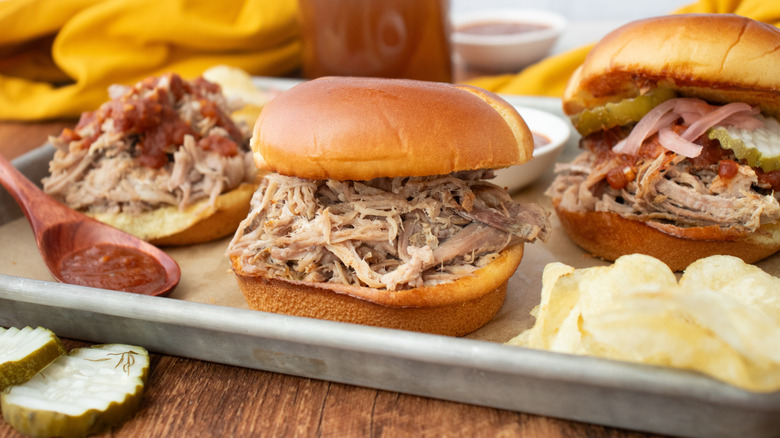 Side shot of pulled pork sandwich with sauces and pickles