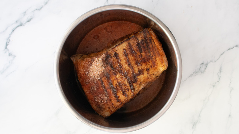 Grilled pork butt in a slow cooker pot with beer and seasoning