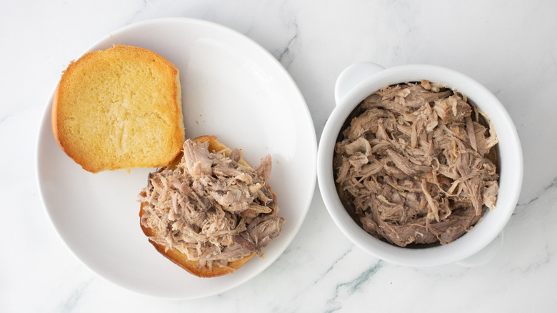 Toasted roll topped with pulled pork on a white plate