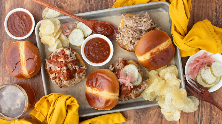 Overhead shot of several pulled pork sandwiches with sauce and pickles