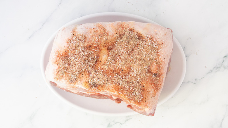 Raw pork butt on a large plate sprinkled with seasonings