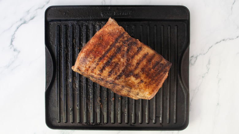 Grilled and seasoned pork butt on a large grill pan