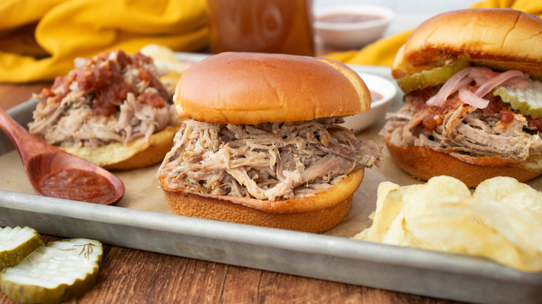 Side shot of pulled pork sandwiches with sauces and pickles