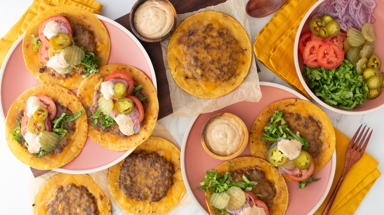 Overhead shot of several smash burger tacos, toppings, and sauce