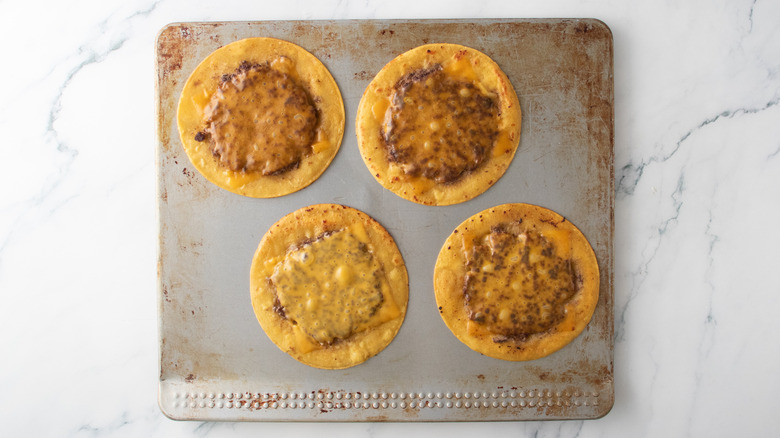 A cookie sheet with four cheesy taco burgers