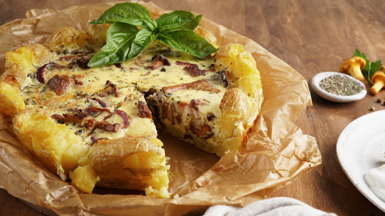 Smashed potato quiche crust with vegetables and fresh basil on wood table.