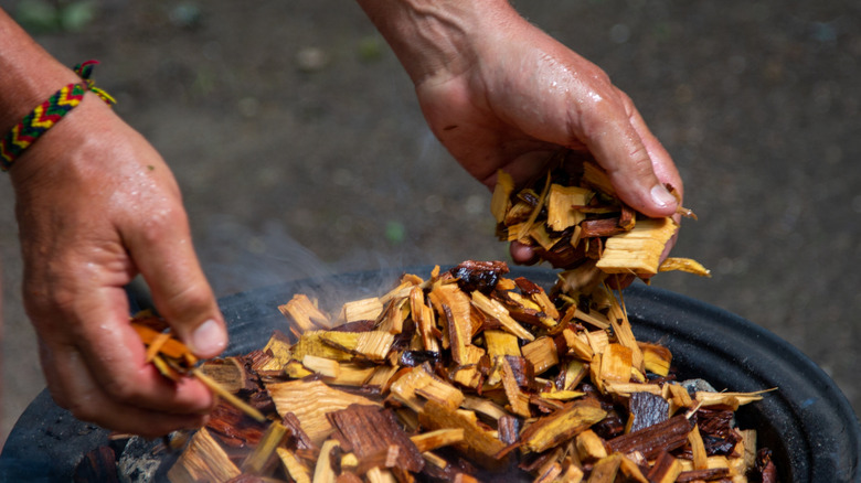 person adding soaked wood to a smoker