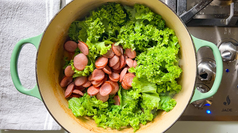 Mustard greens and sliced kielbasa in pot on stove top