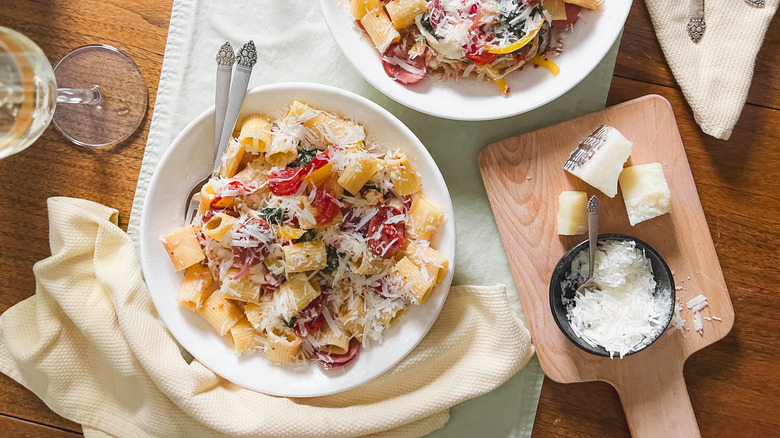 Smoky mustardy kielbasa pasta in serving bowls with grated pecorino on table