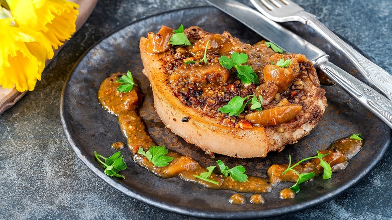 A cooked pork chop covered in sauce, cooked figs, and fresh green herbs on a gray plate