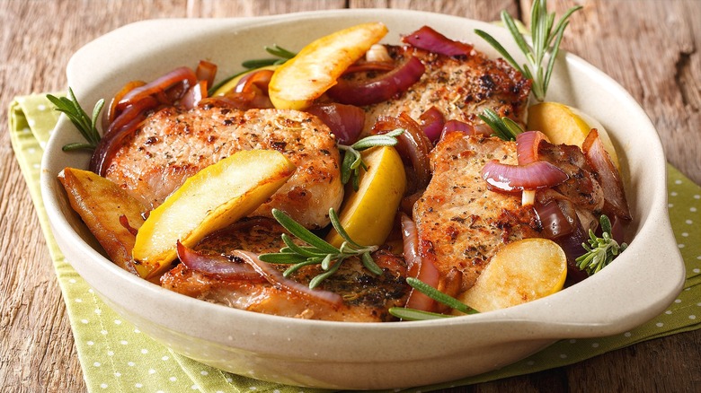 Cooked pork chops with sliced red onions and apples in a shallow and round ceramic baking dish