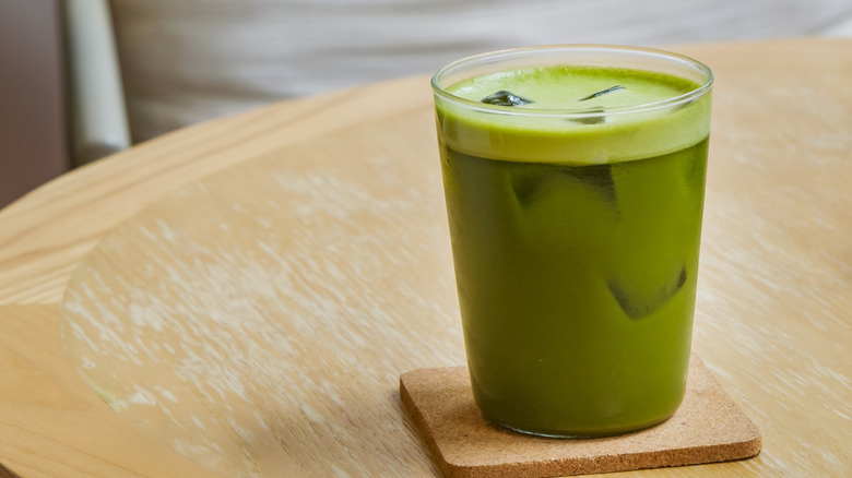 A glass of matcha iced tea sitting on a coaster on a wooden table