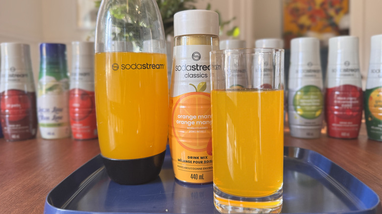 A SodaStream bottle, a syrup bottle and an orange soda glass