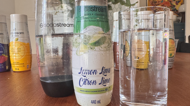 A SodaStream bottle, a syrup bottle and a clear soda glass