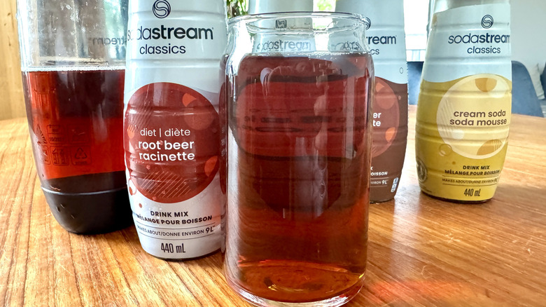 A SodaStream bottle, a syrup bottle and an orange soda glass