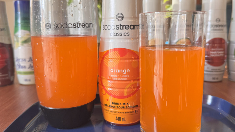 A SodaStream bottle, a syrup bottle and an orange soda glass