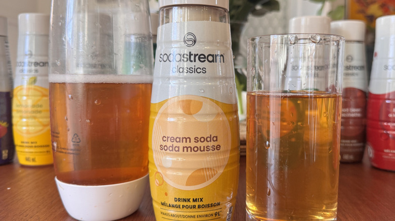 A SodaStream bottle, a syrup bottle and an orange soda glass