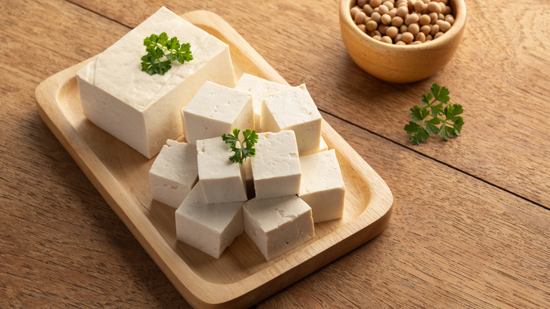 Cubes of soft tofu on a wooden tray with fresh herbs