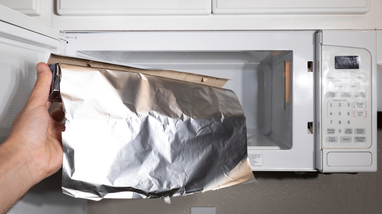 A hand holding aluminum foil in front of an open microwave.