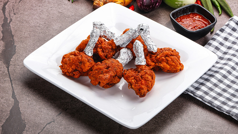 Chicken legs on a plate with their leg bones wrapped in foil.