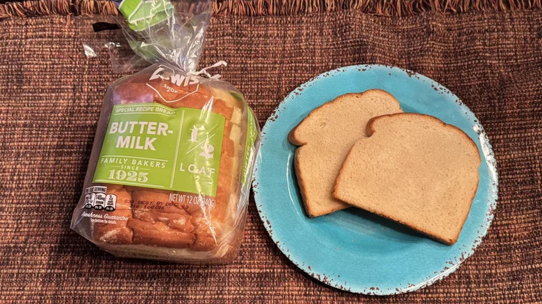 A loaf of Lewis Buttermilk White Bread next to two sliced pieces of bread on a blue plate