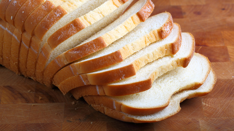 A loaf of sliced white bread on a wood cutting board