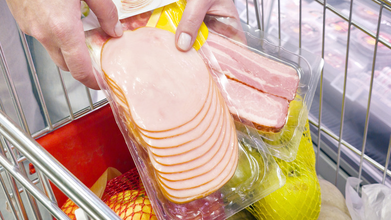Hands holding a package of sliced ham in a shopping cart